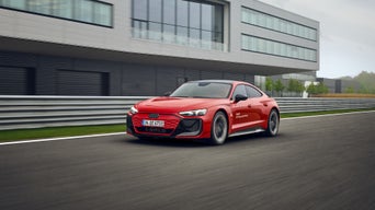 Roter Audi e-tron GT fährt auf Rennstrecke vor modernem Gebäude mit Glasfassade entlang.