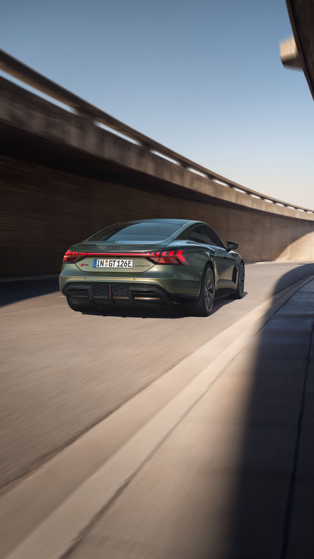 Grüner Audi RS e-tron GT performance von hinten auf einer kurvigen Straße unter einer Betonbrücke.