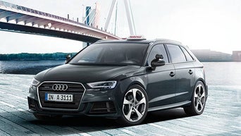 Grauer Audi A3, geparkt an einer Uferpromenade mit einer Brücke im Hintergrund und einem Schild mit der Aufschrift „RSonderfahrzeug” darüber.