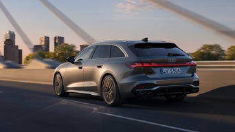 Ein grauer Audi S5 Avant fährt über eine Brücke bei Tageslicht, im Hintergrund Bäume und Hochhäuser.