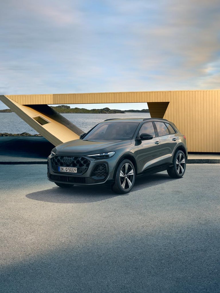 Ein grauer Audi Q5 SUV schräg von vorn vor einem modernen Holzgebäude an einer Wasserstraße.