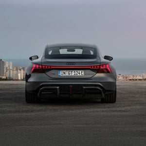Rear view of an Audi RS e-tron GT parked against a coastal city backdrop, showcasing its sleek design and distinctive taillights.