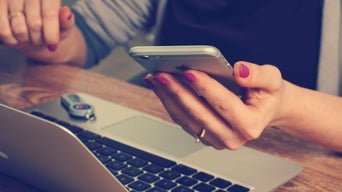 Frau mit Handy in der Hand am Laptop