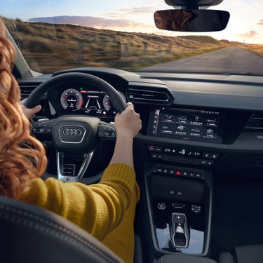 Frau mit beiden Händen am Lenkrad eines Audi A3 allstreet; digitales Cockpit und zentrales Touchdisplay sichtbar.