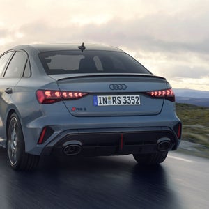 Die RS 3 Limousine von schräg hinten fährt auf einer Gebirgsstraße bei bewölktem Himmel.