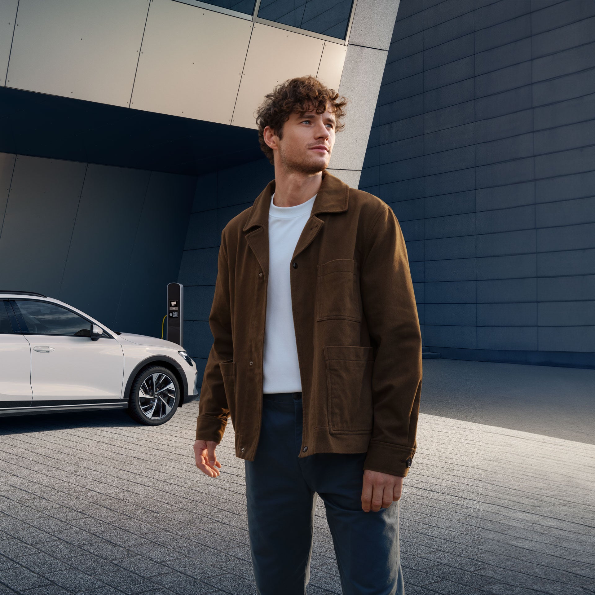Ein Mann steht vor einem modernen Gebäude, hinter ihm steht seitlich ein weißer Audi.