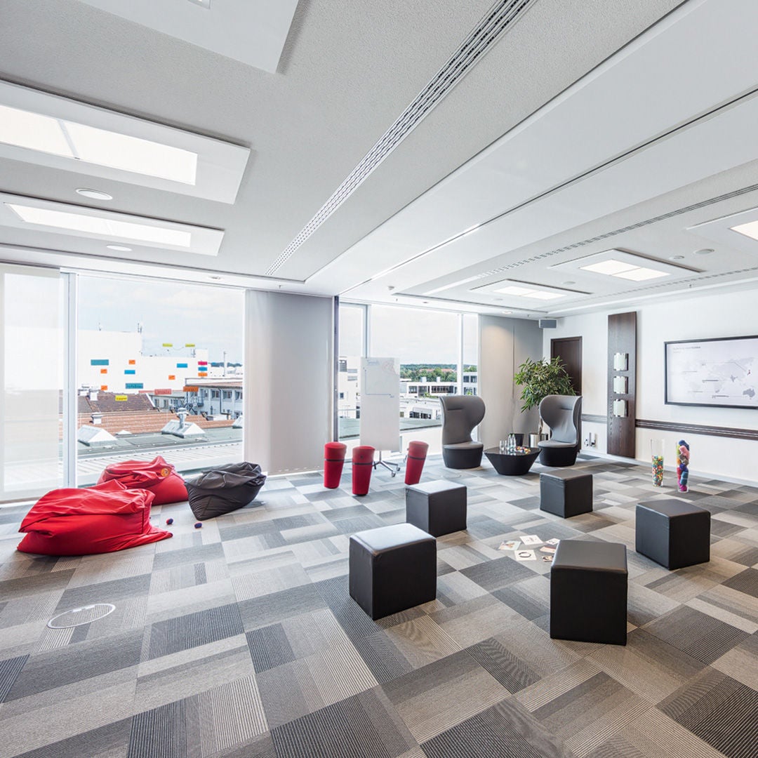 Moderner Raum mit Sitzsäcken, Hockern, Würfelhockern und Blick auf Gebäude durch große Fenster.