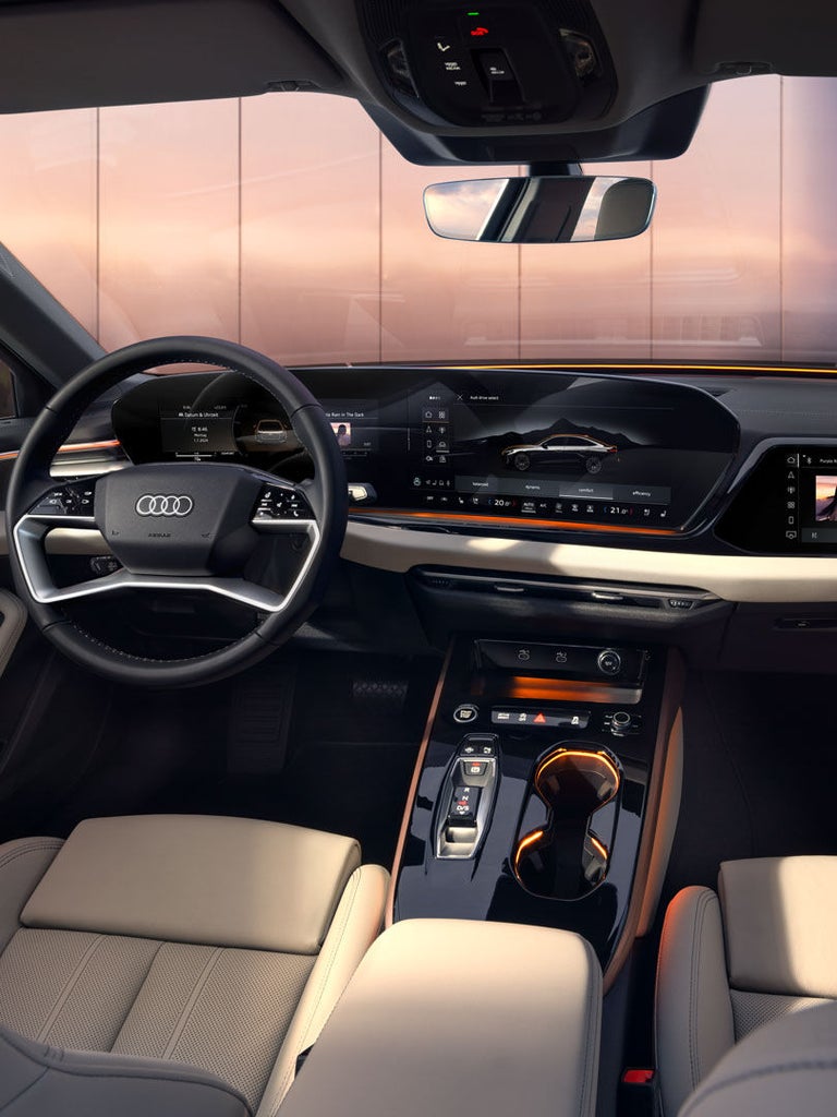 Fahrerin lenkt Audi A5 Limousine mit digitalen Displays, Blick nach vorn auf Straße und Landschaft im Rückspiegel.
