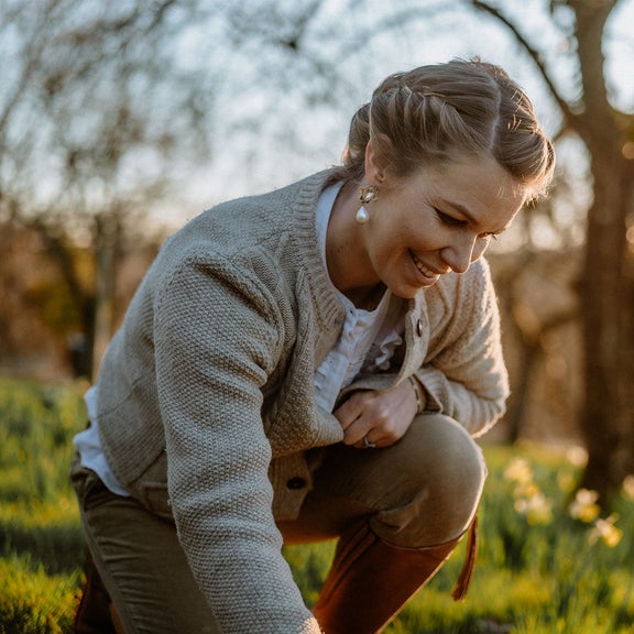 Theresa Baumgärtner kniet auf einer Wiese und pflückt etwas.
