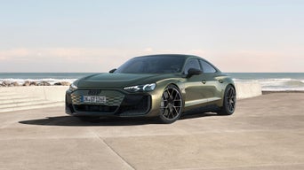 Green Audi RS e-tron GT performance car parked by the ocean, featuring a modern design and striking black wheels against a scenic coastal backdrop.