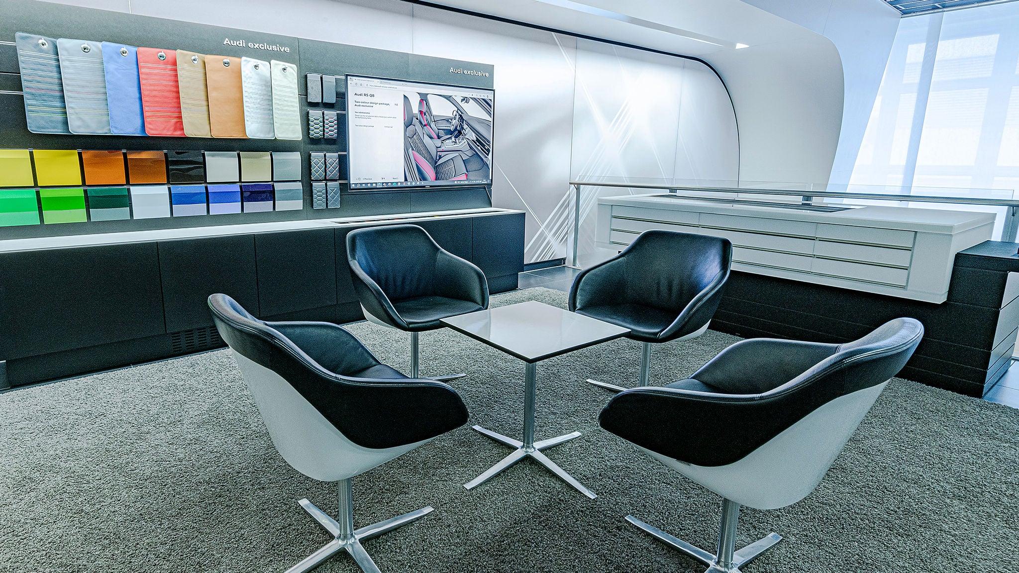 Consultation room with four chairs, color sample wall, and large screen.