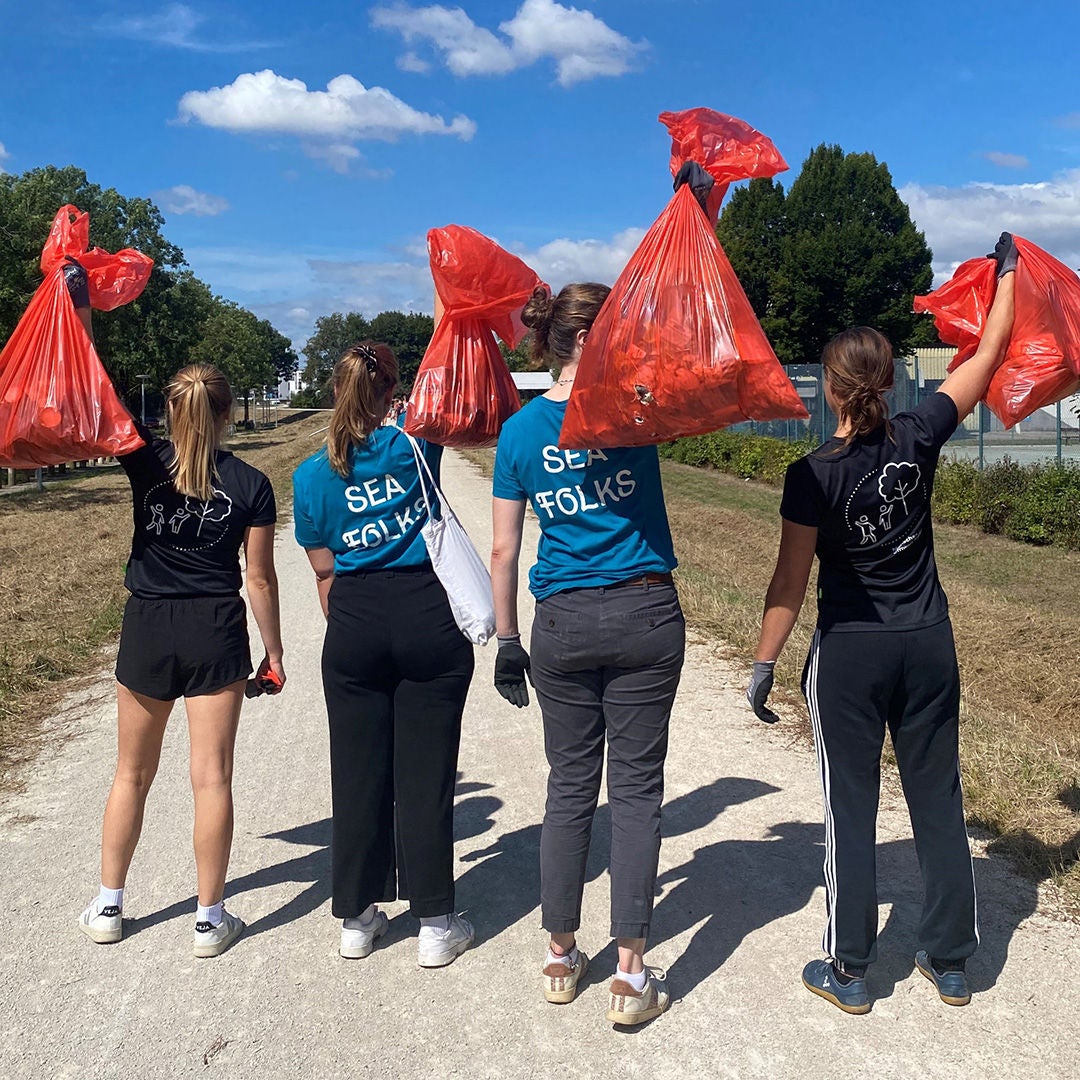 4 teenagers with their backs to the camera lift red rubbish bags filled with rubbish into the air.