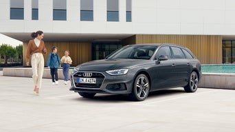 Frau mit zwei Kindern läuft um Audi A4 Gebrauchtwagen herum im Hintergrund ein modernes Haus mit Pool.