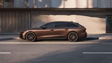 Brauner Audi A6 Avant steht seitlich vor moderner Betonfassade im Schatten auf leerer städtischer Straße.