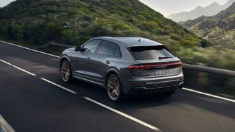 Grauer Audi RS Q8 SUV fährt auf einer kurvigen Straße durch grüne Berglandschaft.