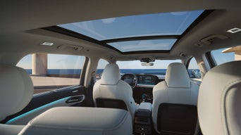 Blick vom Rücksitz auf den Innenraum eines Audi mit Panoramadach und digitalem Cockpit bei Tageslicht.