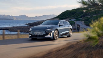 A grey Audi S6 Avant e-tron driving on a coastal road with mountains in the distance.