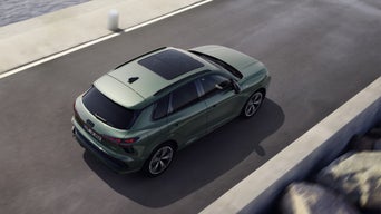 Side profile of a green Q3 SUV parked in front of a house in the city. A young man stands in front of it and opens the passenger door.
