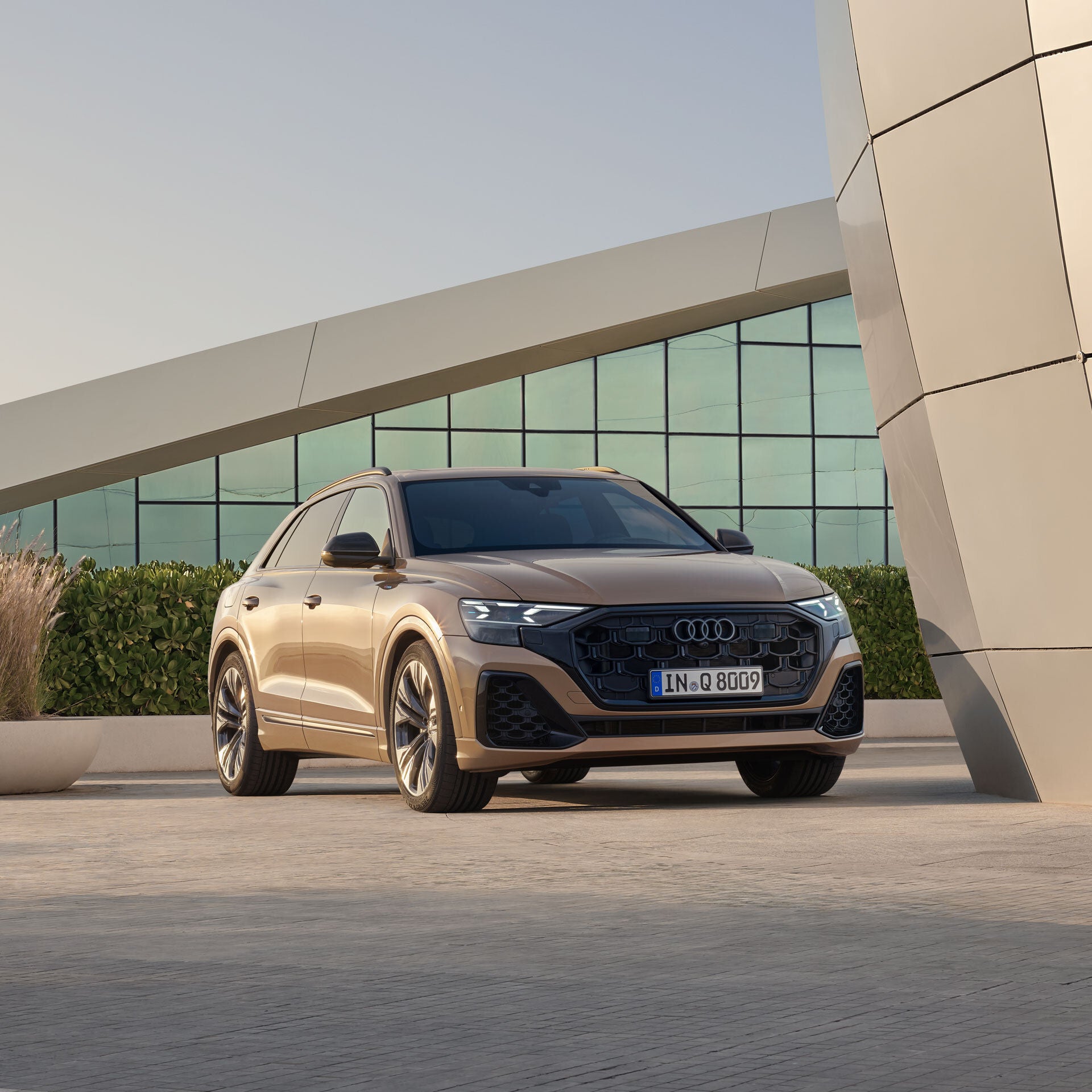 Ein goldener Audi Q8 SUV steht vor einem modernen Gebäude, frontal leicht von der Seite gezeigt.