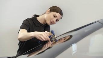 Eine Frau hält ein Gerät an eine Windschutzscheibe eines Audis