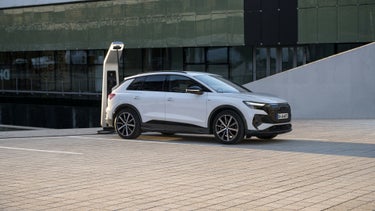 A white Audi Q4 e-tron is parked at a charging station.