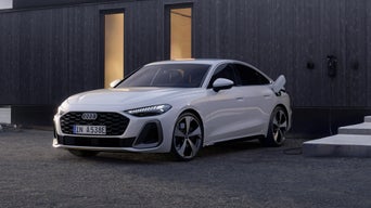 White A5 Sportback e-hybrid stands in front of a modern city building, charging at a station.