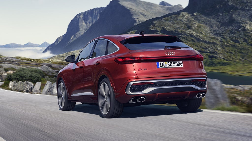 Schräges, hinteres Seitenprofil des roten SQ5 Sportback, welcher auf einer Straße durch die Berge fährt.
