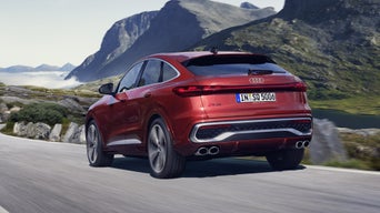 The SQ5 Sportback, seen from an oblique rear angle whilst travelling at full speed along a mountain road. Towering mountains in the background.