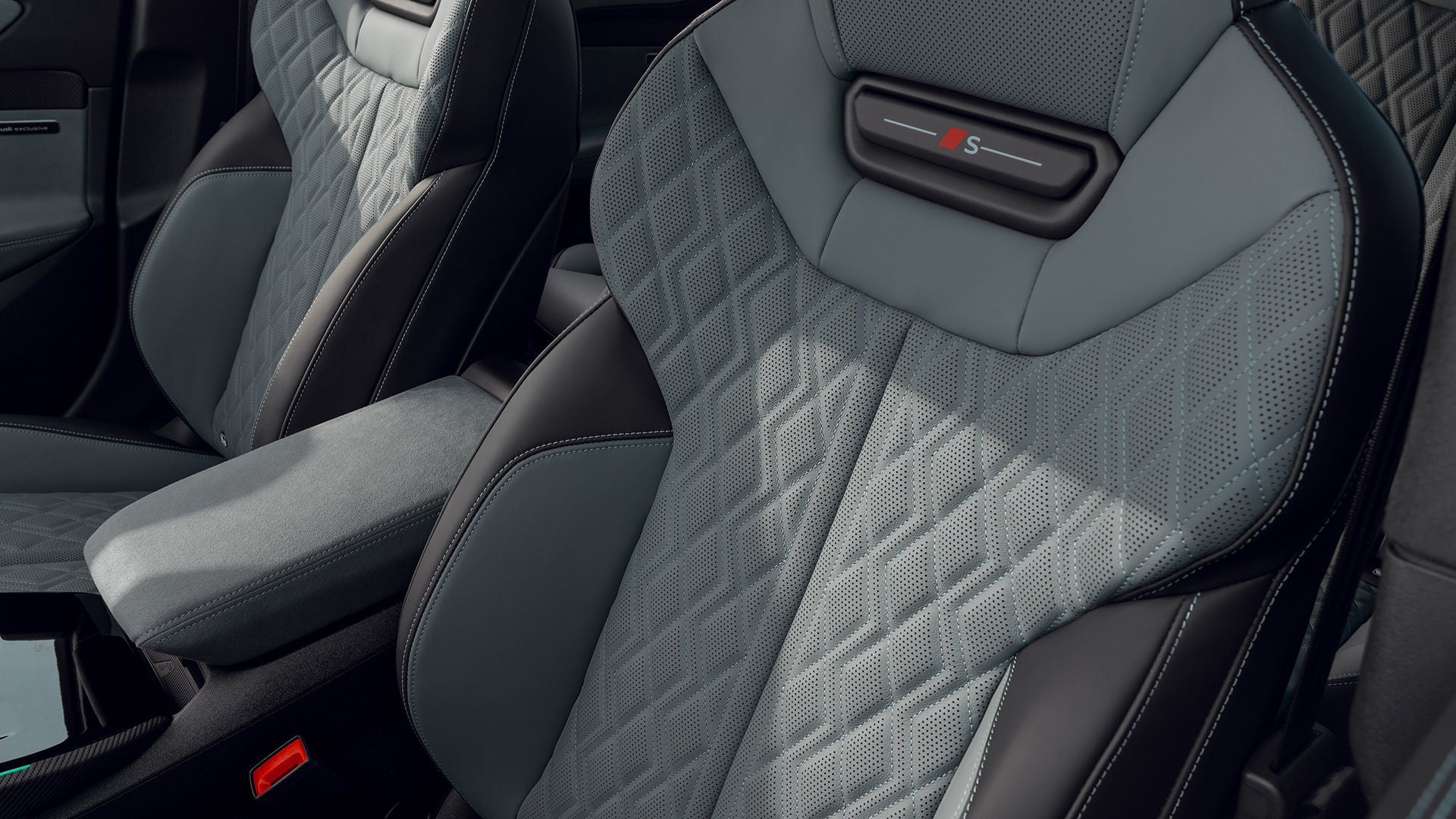 Close-up of two gray-green sports seats with diamond stitching and S emblem in an Audi A6 sedan; armrest in the middle.