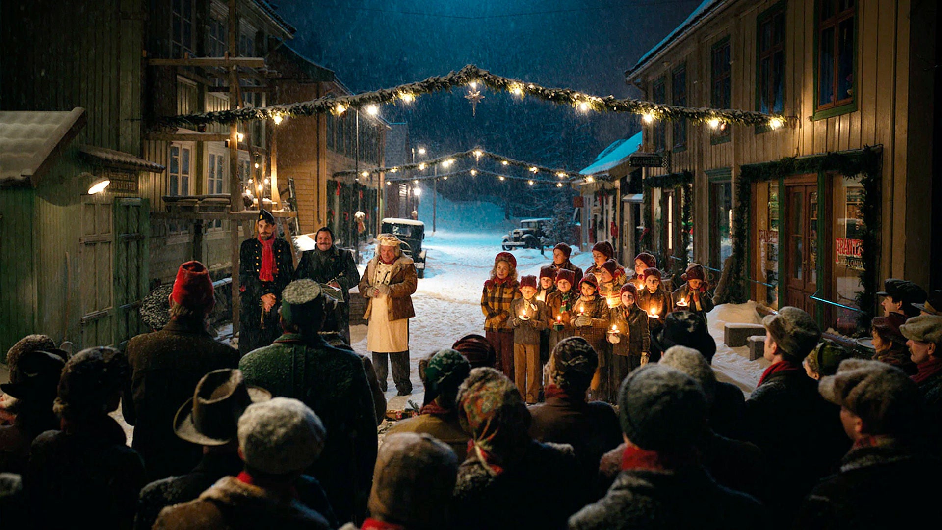 Kinder und Erwachsene mit leuchtenden Kerzen singen auf der Strasse im Schnee Weihnachtslieder. 