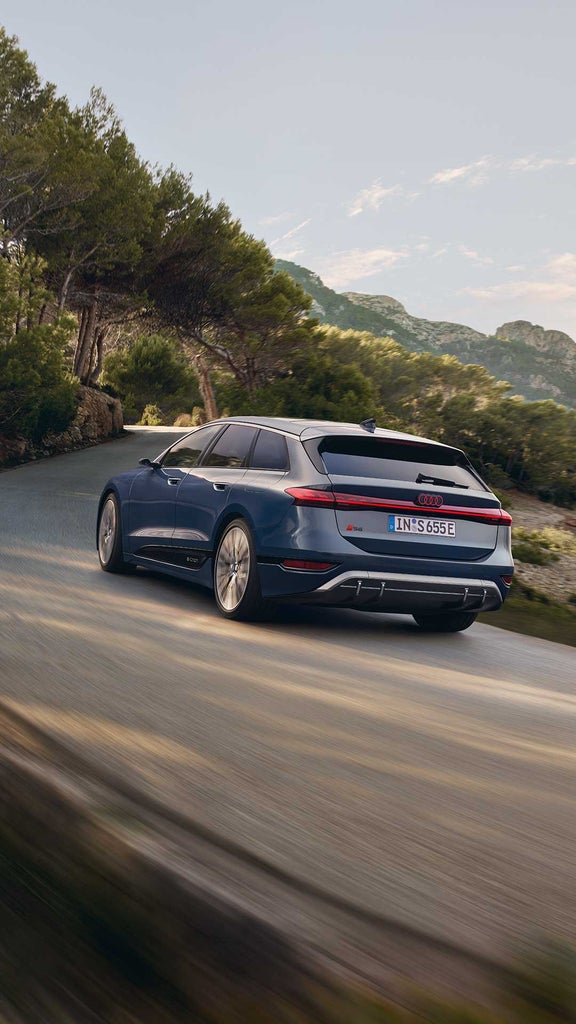 Dunkelblauer Audi S6 Avant e-tron fährt auf einer kurvigen Straße durch eine bergige Landschaft.