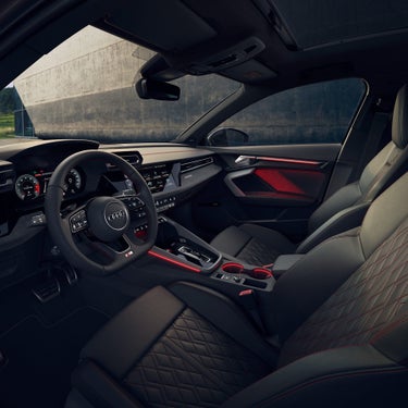 Blick in den Audi-Innenraum mit Lenkrad, Displays und blauer Ambientebeleuchtung bei Sonnenuntergang.