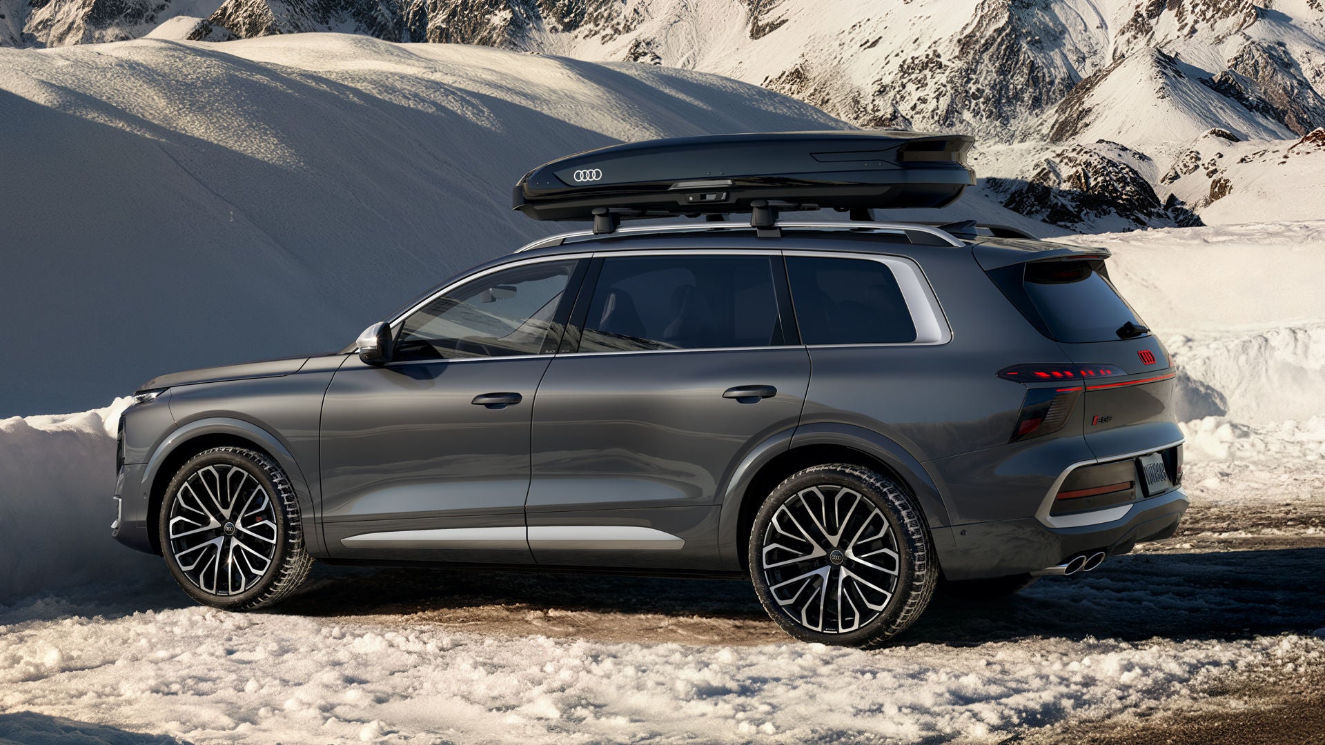 The Audi SQ9 SUV, seen slightly from the side in a parking lot surrounded by a snowy landscape. There is a roof box on the roof.