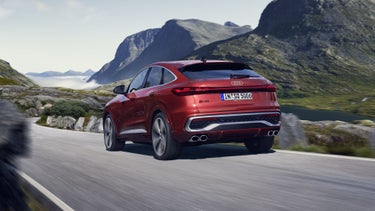 Schräges, hinteres Seitenprofil des roten SQ5 Sportback, welcher auf einer Straße durch die Berge fährt.