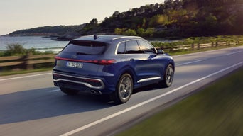 Schräge, seitliche Heckaufnahme des SQ5 SUV in dunkelblau, welcher auf einer Straße entlang der Küste fährt.