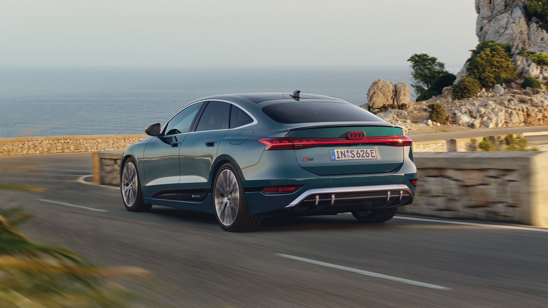 Audi S6 Sportback e-tron drives along a scenic coastal road, showcasing its sleek design against a backdrop of ocean and rocky cliffs.