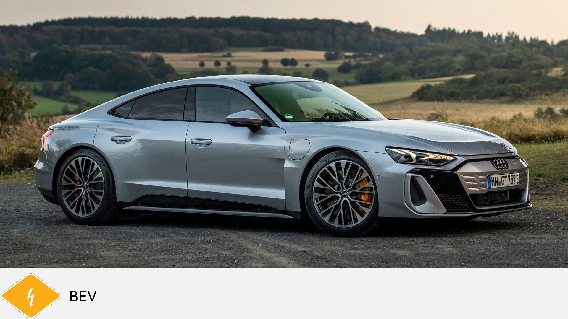 Silver Audi RS e-tron GT standing on a country lane in front of a meadow and forest. Yellow BEV symbol with lightning bolt below.