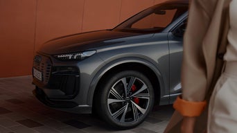 A grey Audi SUV parked against a warm orange wall, showcasing its stylish design and sporty black alloy wheels.