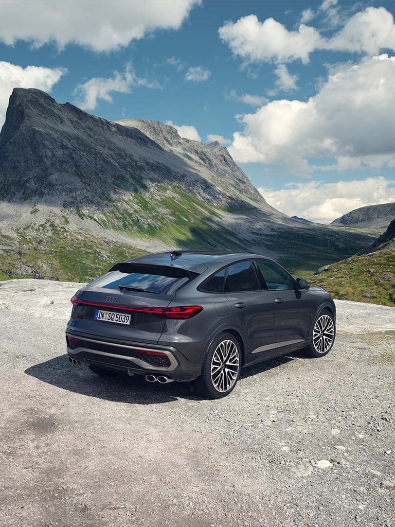 Ein grauer Audi SQ5 Sportback von schräg hinten auf felsigem Untergrund in grüner Gebirgslandschaft.