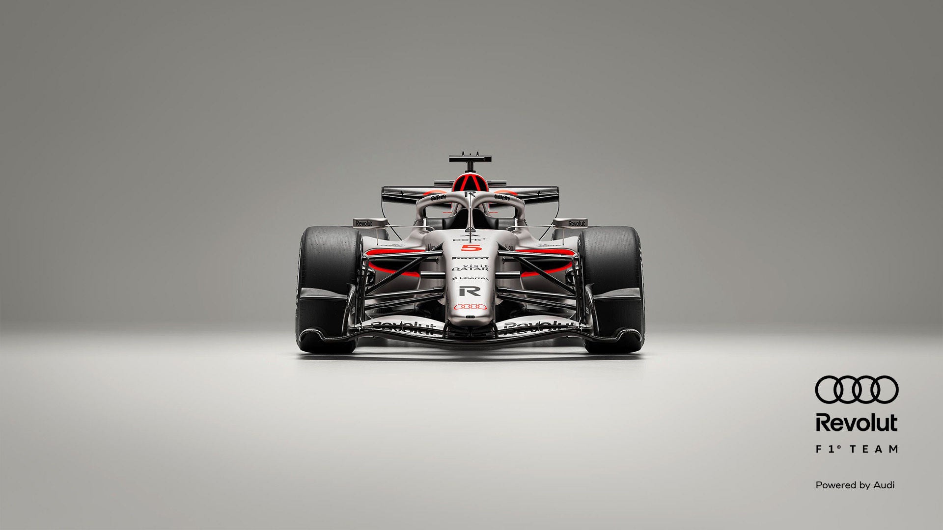 Frontansicht eines silber-schwarzen Formel-1-Rennwagens mit roten Akzenten vor grauem Hintergrund, Audi- und Revolut-Logo in schwarz am Rand.