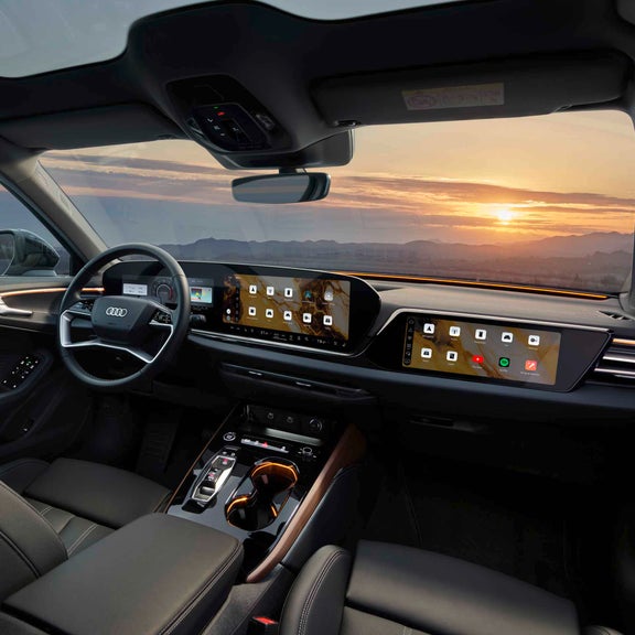 Interior moderno de un Audi con iluminación ambiental violeta, una gran pantalla táctil y la fachada dorada de un edificio al fondo.