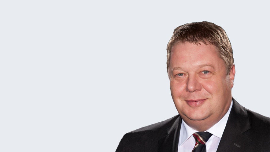 Michael Molitoris: Porträt eines älteren, freundlich schauendem Mann im Anzug vor grauem Hintergrund.