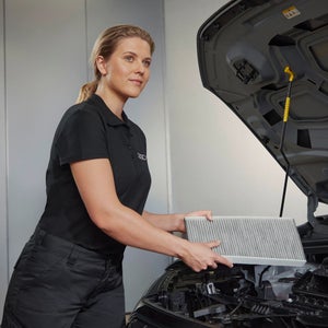 A mechanic holding an air filter in front of an open car bonnet
