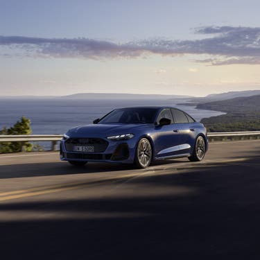 Die S5 Limousine in dunkelblau fährt auf einer Straße entlang der Küste.