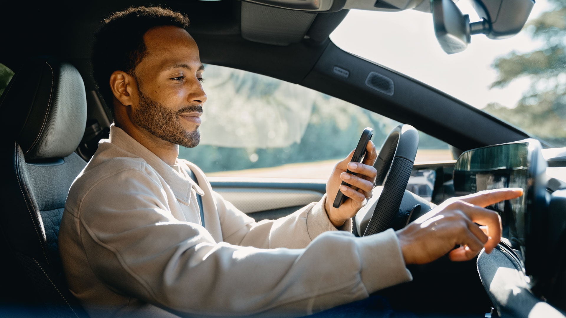 A man is sitting behind the wheel of his Audi. He is holding his smartphone in one hand while operating the vehicle's MMI with the other.