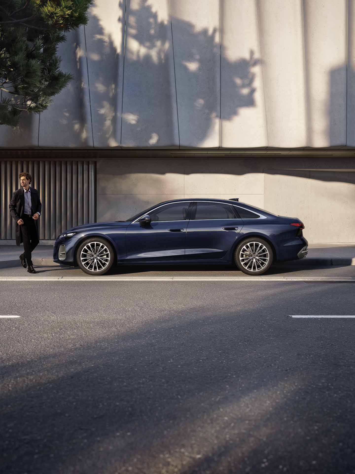 Die A6 Limousine im Seitenprofil in einer Parkbucht vor der Fassade eines Gebäudes. Vor dem Fahrzeug steht ein junger Mann.