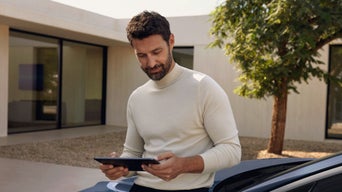 Silhouette eines Mannes mit Smartphone hinter Glasfront, Spiegelung von Pflanzen und Landschaft im Fenster sichtbar.