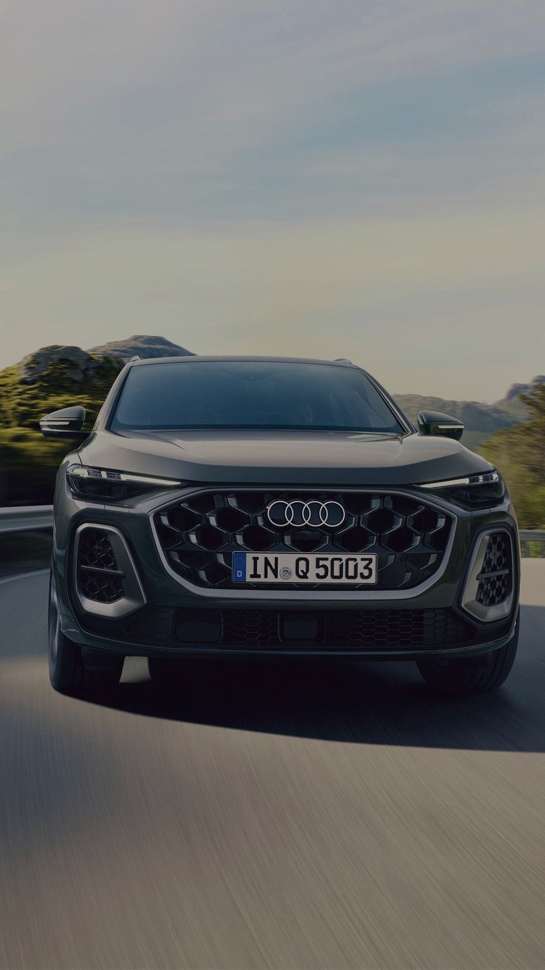 A grey Audi SUV parked near a modern building with a coastal backdrop.