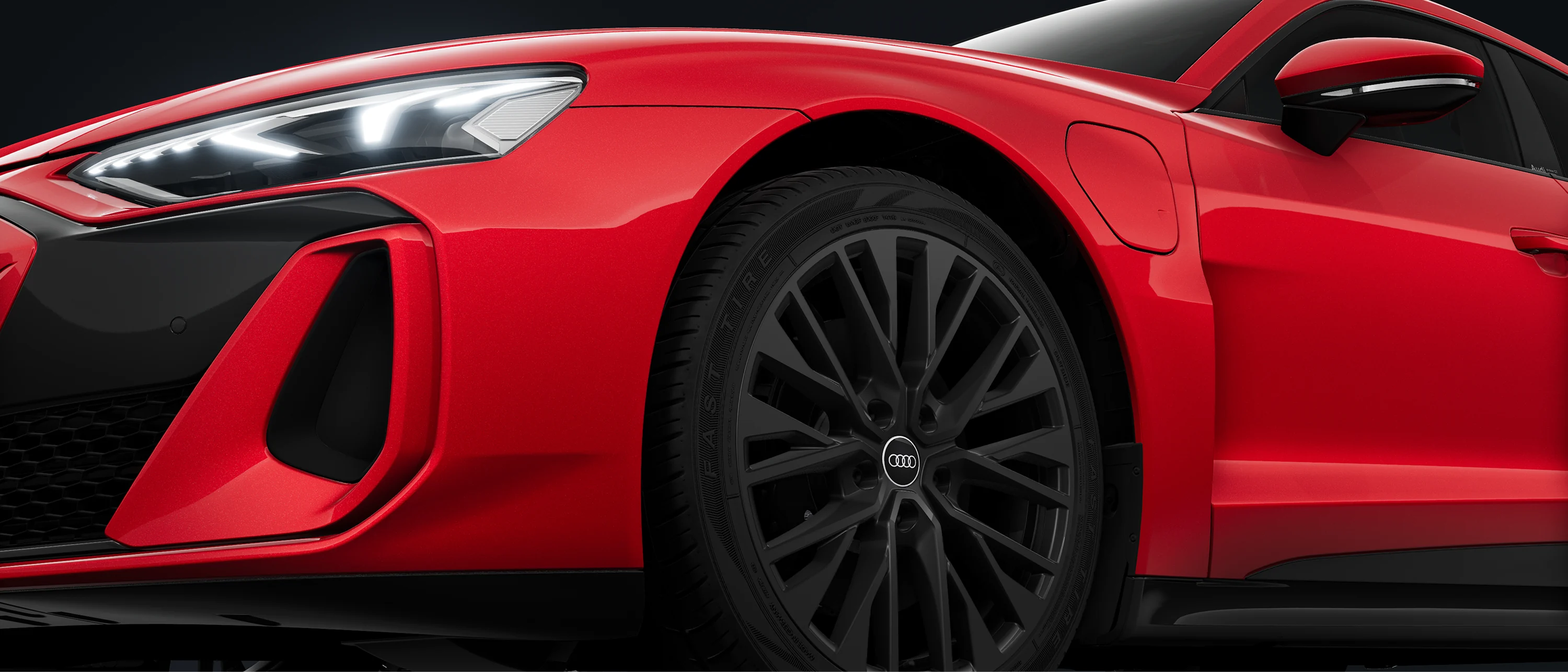 Close-up of red Audi e-tron gt quattro front wheel and LED headlight against a dark background