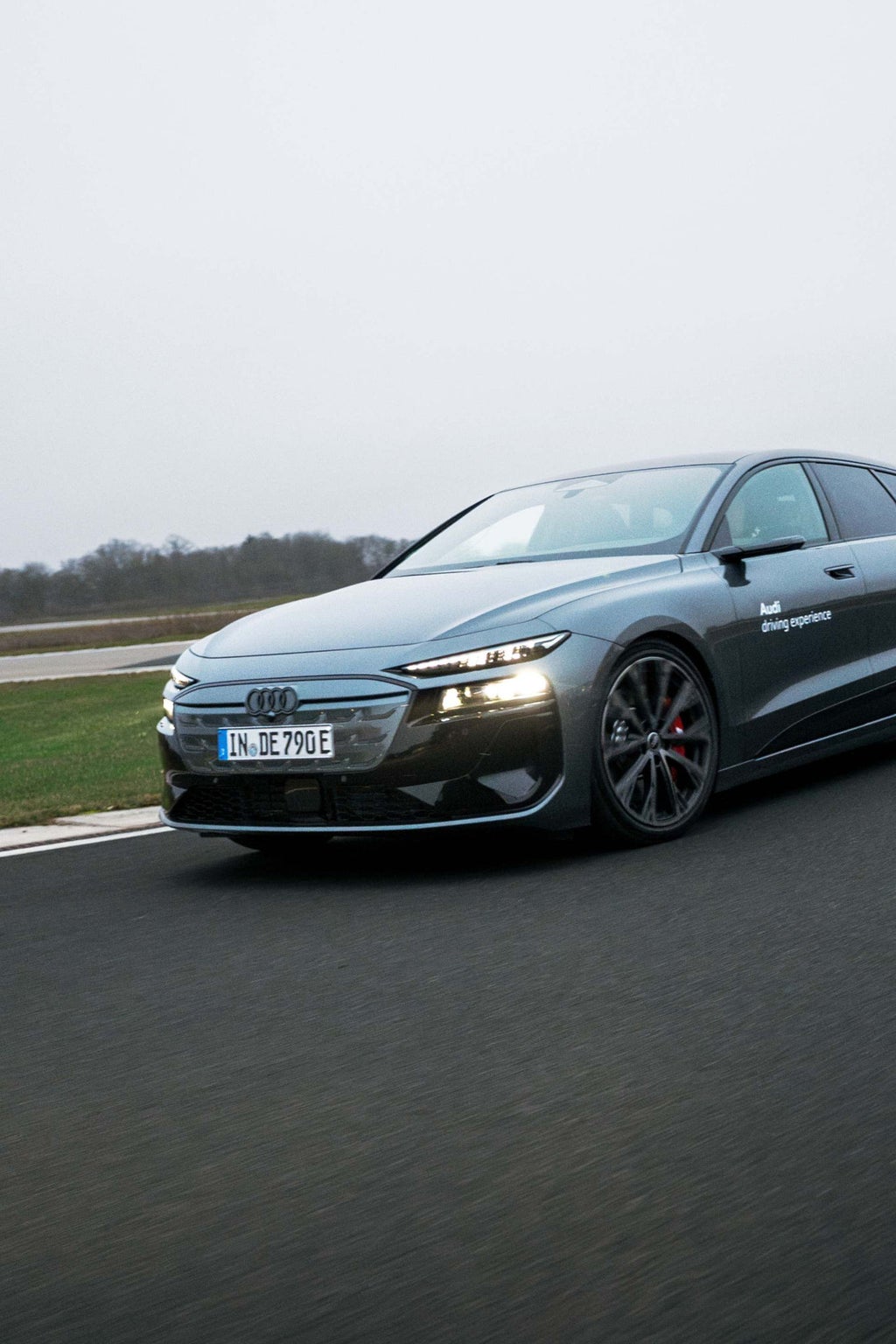 Schräge Frontansicht des Audi S6 Avant e-tron auf der Teststrecke von Audi driving experience mit beleuchteten Scheinwerfern.